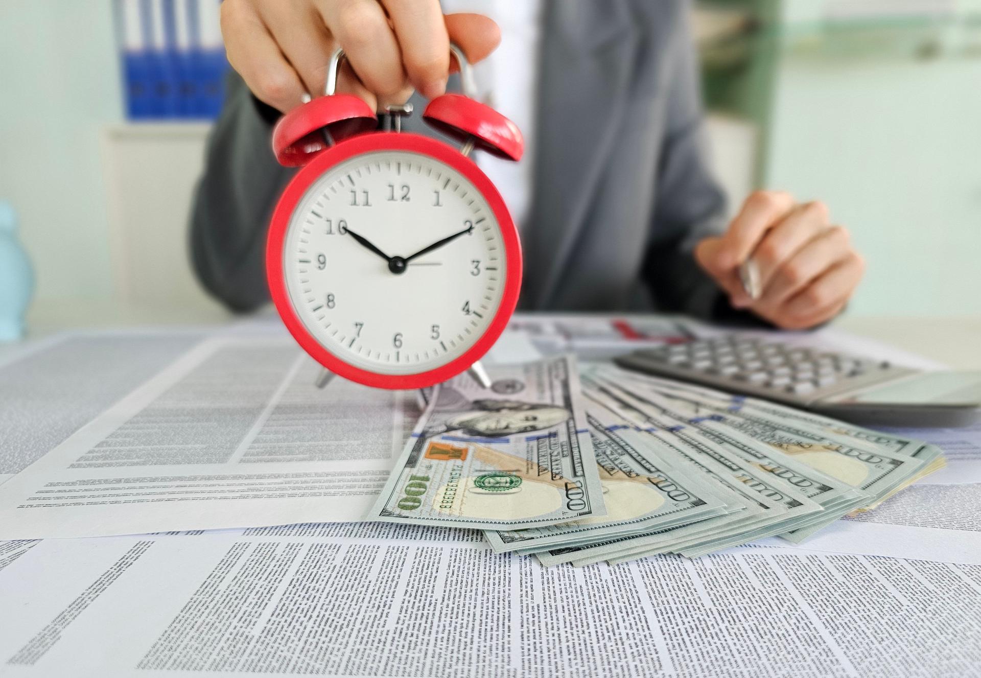 Clock held over financial documents with cash, calculator, and paperwork during a business meeting concept